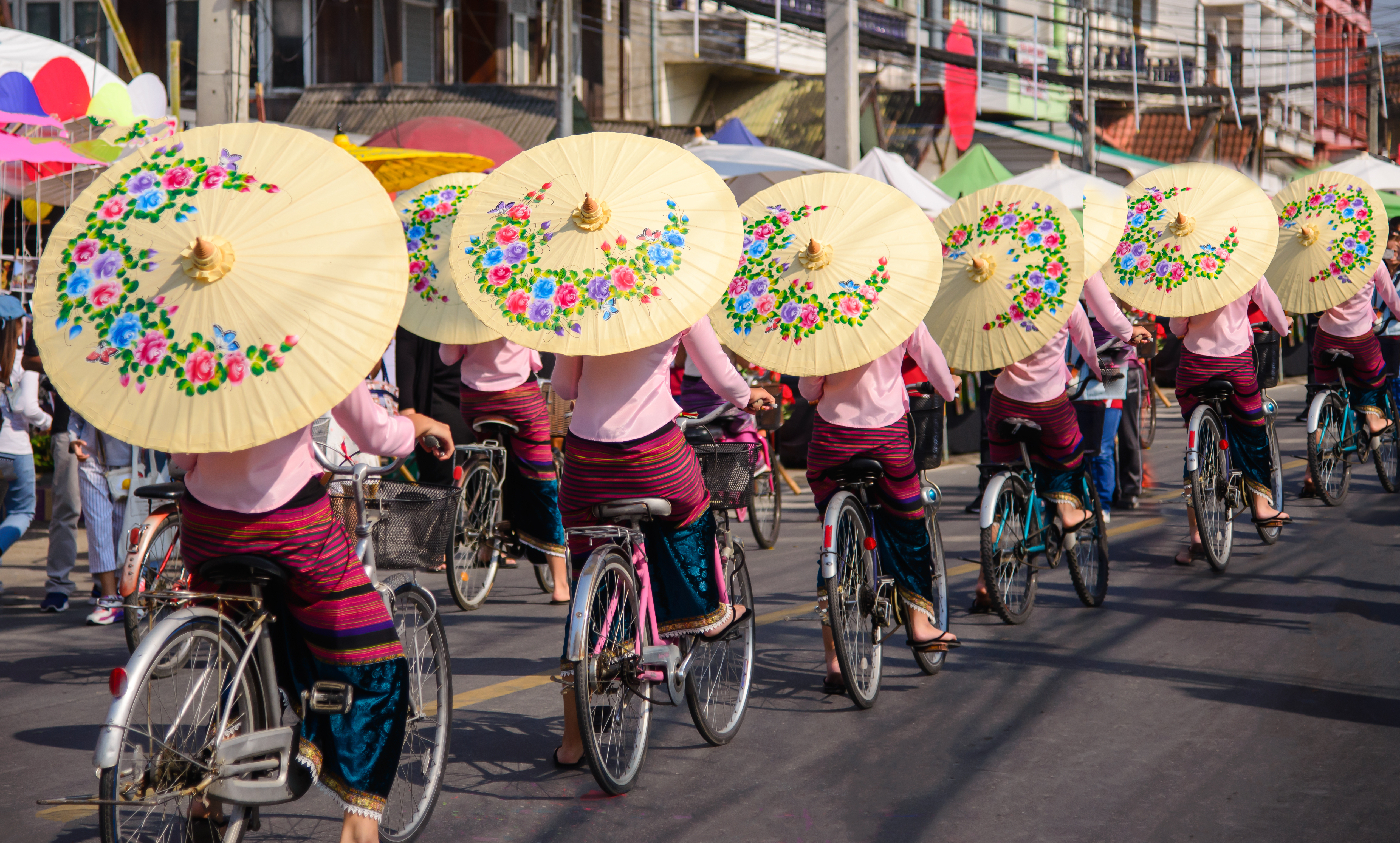 Women on bicycles holding umbrellas in Bo Sang, Chiang Mai